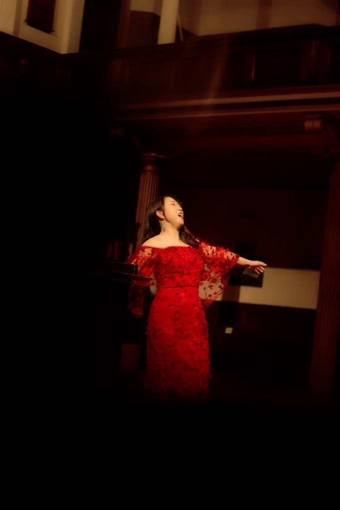 Aleta Shang singing in a red gown during a recital